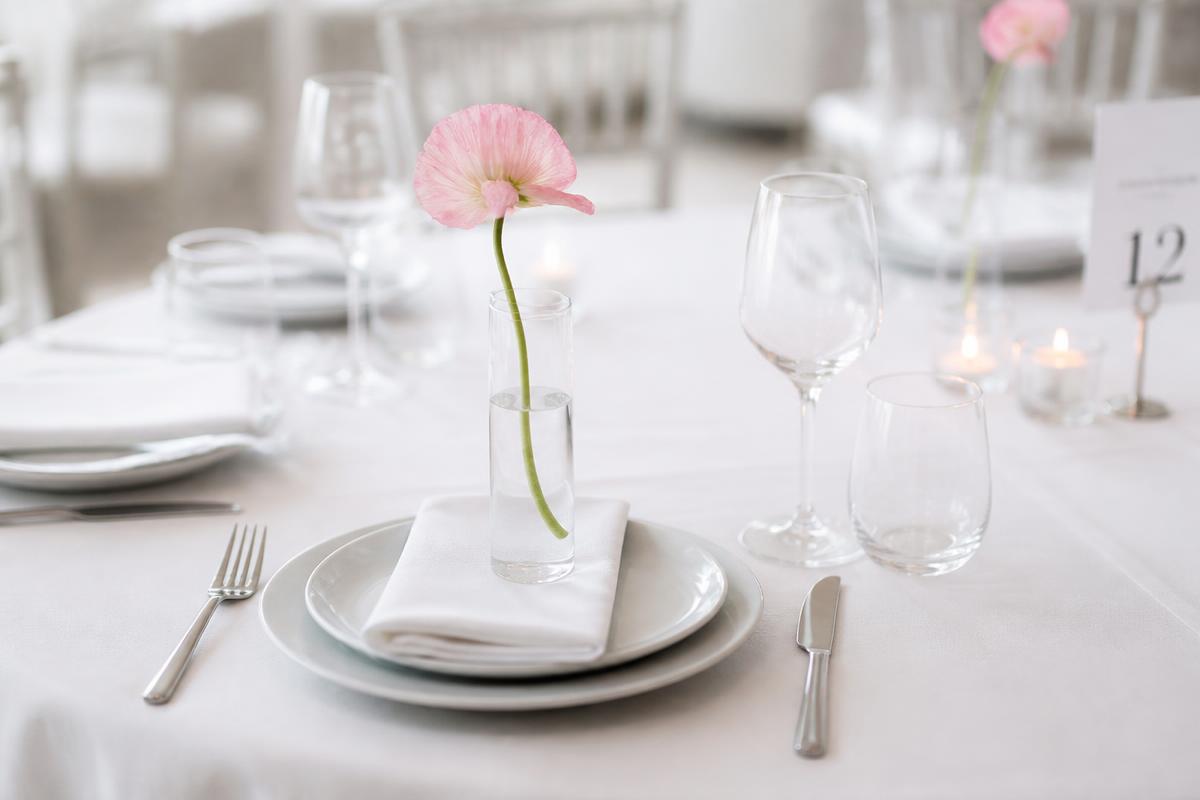 Elegant corporate gala table setting with white linens and a single pink flower